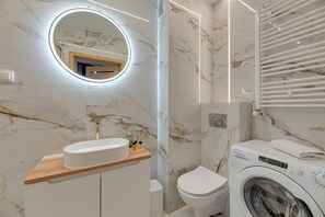 Ein Badezimmer mit Marmorwand, einem runden Spiegel, einem Waschbecken, einer Toilette und einer Waschmaschine.