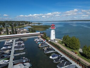 Un puerto deportivo con barcos amarrados, un faro y una zona residencial con casas y árboles.