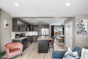 Una cocina moderna con armarios oscuros, una isla central y una zona de comedor con mesa y sillas.