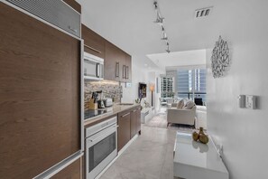 Une cuisine moderne avec des meubles en bois, un four encastré et un coin repas comprenant une table et des chaises blanches.