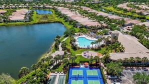 Eine Vogelperspektive eines Resorts mit einem zentralen Schwimmbad, Tennisplätzen und einem See.