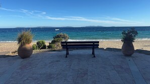 A bench overlooking a beach with a clear view of the sea and distant land. - QUIET ACCOMMODATION CLOSE TO BEACHES AND SHOPS (Le Lavandou)