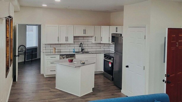 Una cocina moderna con armarios blancos, una isla central y un sofá azul en un amplio salón.