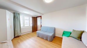A room with a sofa, a small table, a window with curtains, and a radiator. - Little ingersheim near Colmar (Ingersheim)