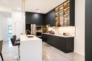 Een moderne keuken met zwarte kastjes, roestvrijstalen apparatuur en een wit aanrecht.