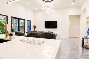 Een moderne keuken met een marmeren eiland, een zithoek met een bank en een aan de muur bevestigde televisie.