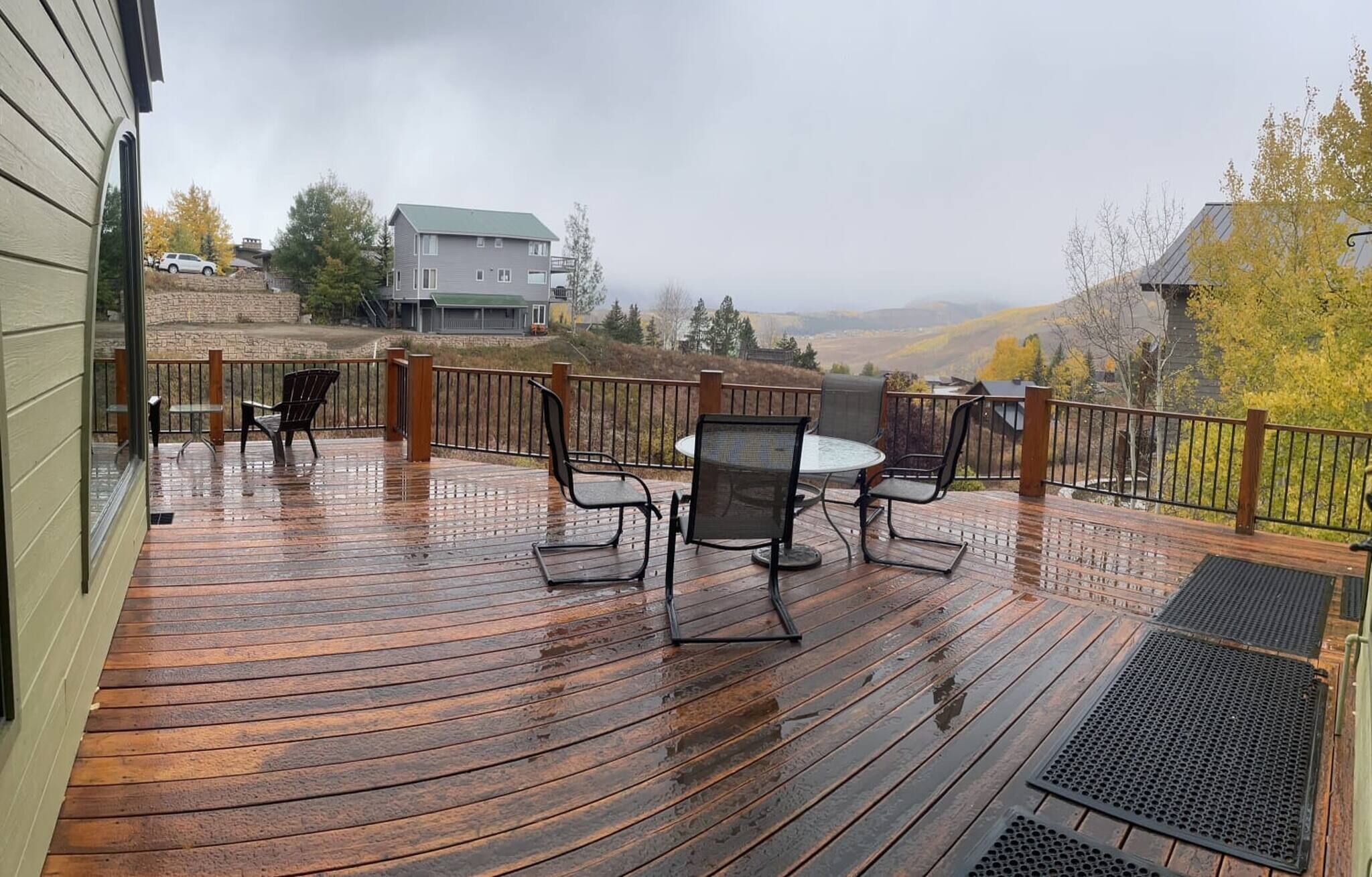 A wooden deck with outdoor furniture, a railing, and a view of a hilly landscape.