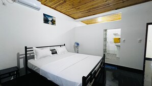 A bedroom with a wooden ceiling, a bed with white bedding, a wall-mounted air conditioner, and a bathroom visible through an open door. - Apartment no. 4 (Antsiranana)