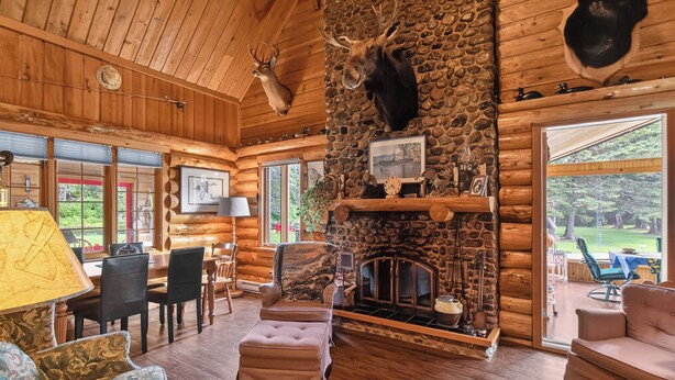 A log cabin interior with a stone fireplace, mounted animal heads, and a dining area. -  Waterfront Log Cabin for Nature Lovers,moments with family friends, Spa Sleep 8 (Wayerton)