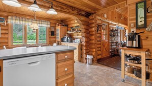 A log cabin kitchen with a dishwasher, wooden cabinets, and a stone floor. -  Waterfront Log Cabin for Nature Lovers,moments with family friends, Spa Sleep 8 (Wayerton)