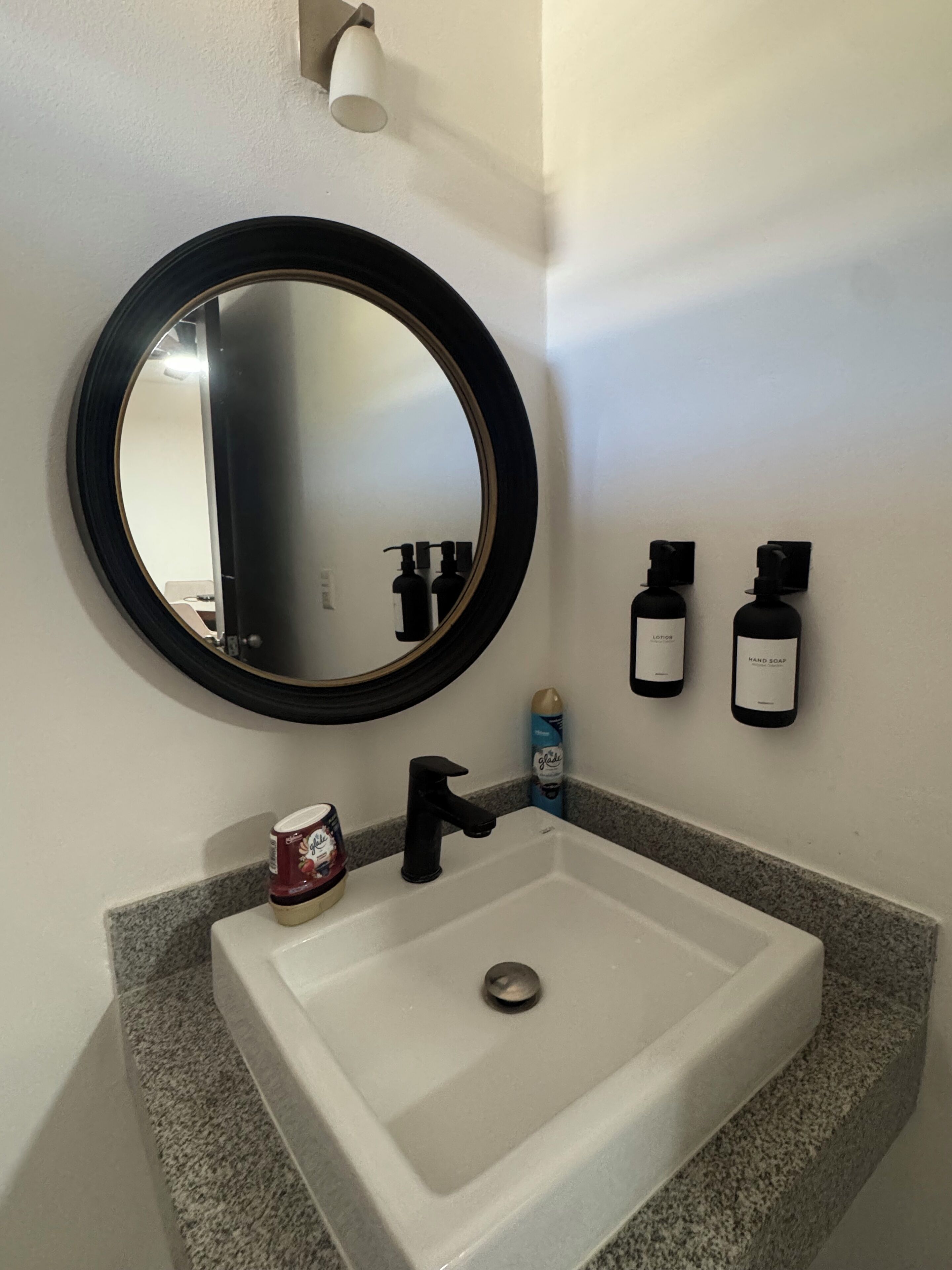 A bathroom with a white sink, a round mirror, and two bottles of hand soap.