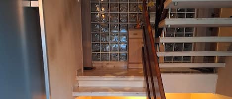 Un escalier avec une rampe en bois, des marches en marbre et un mur en blocs de verre en haut.