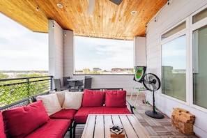 A balcony with a wooden ceiling, a red sofa, a table, and a fan. - Penthouse Paradise Riverwalk Views Rooftop View (San Antonio)