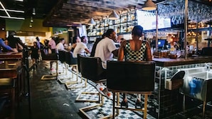A bar with tables and chairs, a counter, and shelves with bottles.
