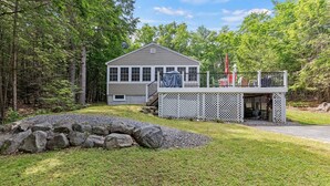 A two-story house with a deck, surrounded by a natural landscape. - Cozy 2-bedroom cottage in charming Frye Island-Four minute walk to the beach (Frye Island)