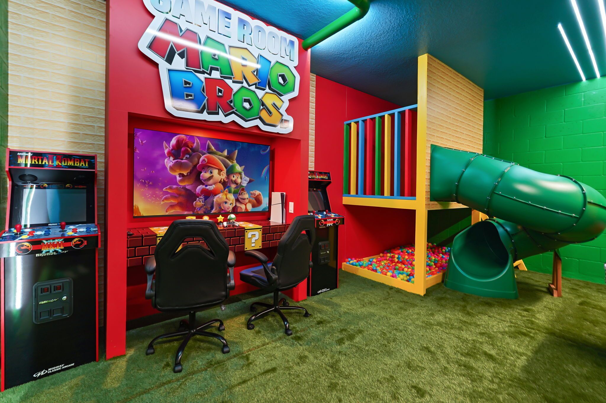 Habitación temática de Mario con juegos de arcade, un escritorio, sillas, un tobogán verde y una piscina de pelotas.