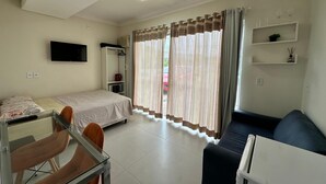Habitació d'hotel amb un llit, una taula de treball amb una cadira, un sofà, una televisió penjada a la paret i una finestra amb cortines.
