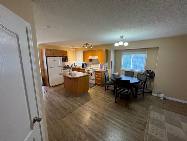 A kitchen with wooden cabinets, a central island, a dining table with chairs, a ceiling fan, and a window with blinds.