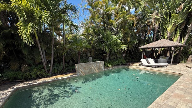 Ein Pool mit Steinmauer, umgeben von üppigen tropischen Pflanzen und einem hölzernen Pavillon.
