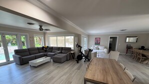 Ein geräumiger Wohnbereich mit einem gro ßen Esstisch aus Holz, einem grauen Ecksofa und einem Deckenventilator.