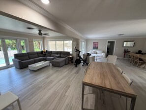 Ein geräumiger Wohnbereich mit einem großen Esstisch aus Holz, einem grauen Ecksofa und einem Deckenventilator.