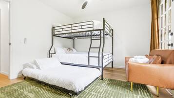 Un lit superposé, un tapis à rayures vertes, un fauteuil en cuir marron et un ventilateur de plafond.