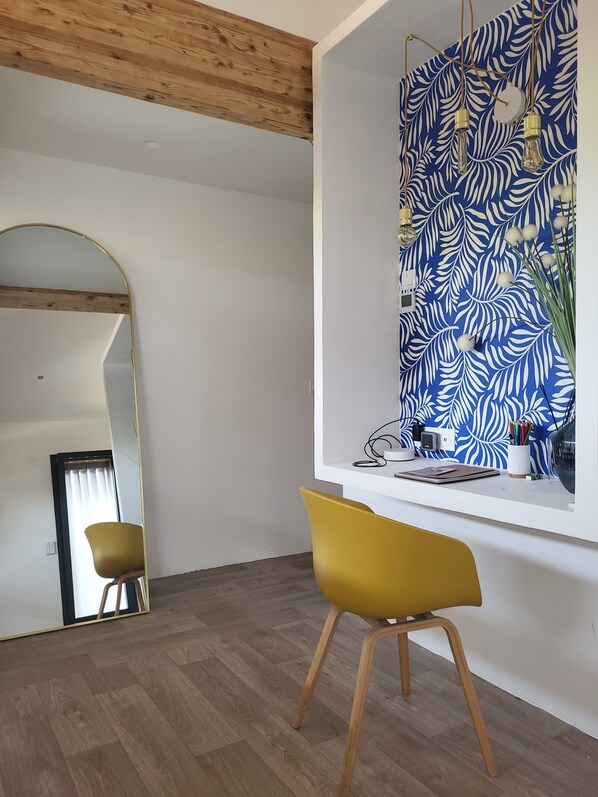 Une chambre moderne avec un plafond en bois, un grand miroir, une chaise jaune et un mur orné d’un motif de feuilles.