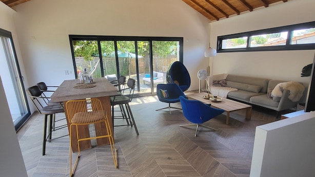 A spacious room with a herringbone-patterned floor, a dining area with a table and chairs, a sofa, and a ceiling fan. - Family home (Le Teich)