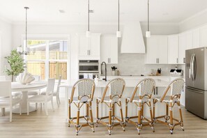 Eine moderne Küche mit weißen Schränken, einem Edelstahl-Kühlschrank und einem Essbereich mit weißen Stühlen und einem Tisch.