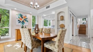 A dining area with a wooden table and chairs, a chandelier, and a large window with a view of greenery. - Newly Refreshed Luxury Villa End Unit at The Islands at Mauna Lani M4 (Waimea)
