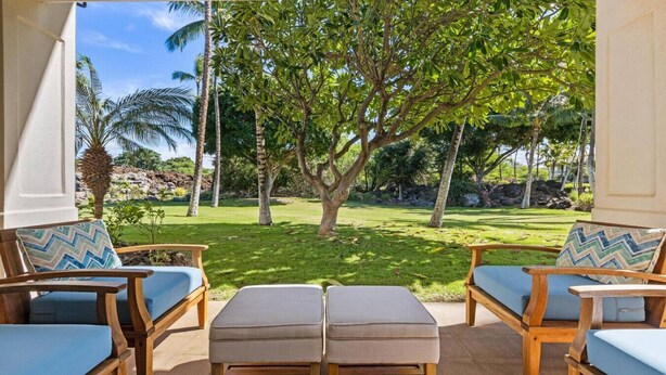 A covered outdoor seating area with wooden furniture and a view of a lush garden. - Newly Refreshed Luxury Villa End Unit at The Islands at Mauna Lani M4 (Waimea)