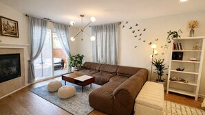 Uma sala de estar com um sofá seccional marrom, uma mesa de centro de madeira, uma lareira e uma estante de livros.