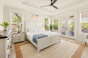 A bedroom with a bed, nightstands, a dresser, a ceiling fan, and large windows. - 4BR Beach Luxury • Pool, Hot Tub + Game Room (Jacksonville Beach)