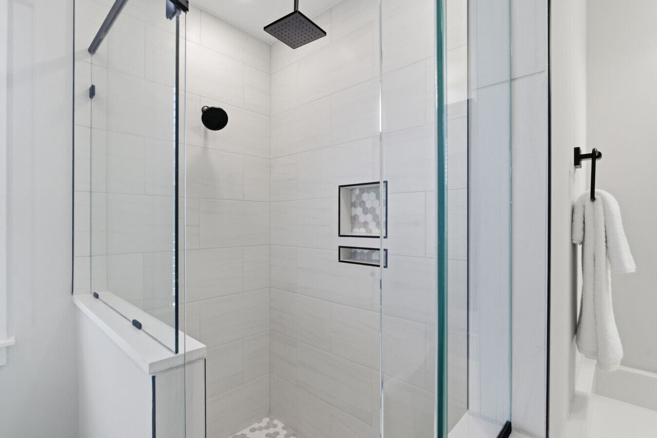 A glass-enclosed shower with a square showerhead, a glass door, and a towel rack with a towel.