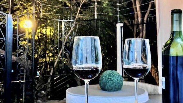 Deux verres à vin sont posés sur une table, à côté d’une bouteille, le tout étant entouré de guirlandes lumineuses et de lanternes suspendues.