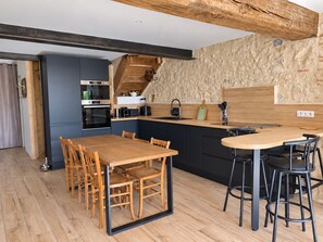 Una cocina moderna con una mesa y sillas de madera, horno empotrado y salpicadero con textura de piedra.