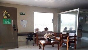 A reception area with a reception desk, a waiting area with chairs and a table, a door with a sign, and a window with a view. - Hotel Pousada das Palmeiras (Colider)