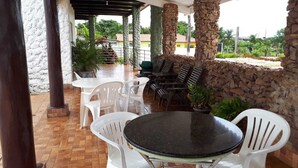 An outdoor patio with stone pillars, white plastic chairs, and tables. - Hotel Pousada das Palmeiras (Colider)