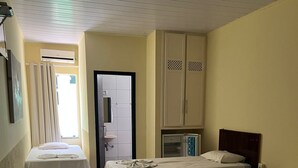 A hotel room with three beds, a microwave, a TV, and a door leading to a bathroom. - Hotel Pousada das Palmeiras (Colider)