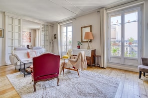 A spacious room with a red chair, a sofa, a small table, and a view of the outside through large windows. - Bright Oasis in the Heart of Montmartre - Elevator (Paris)
