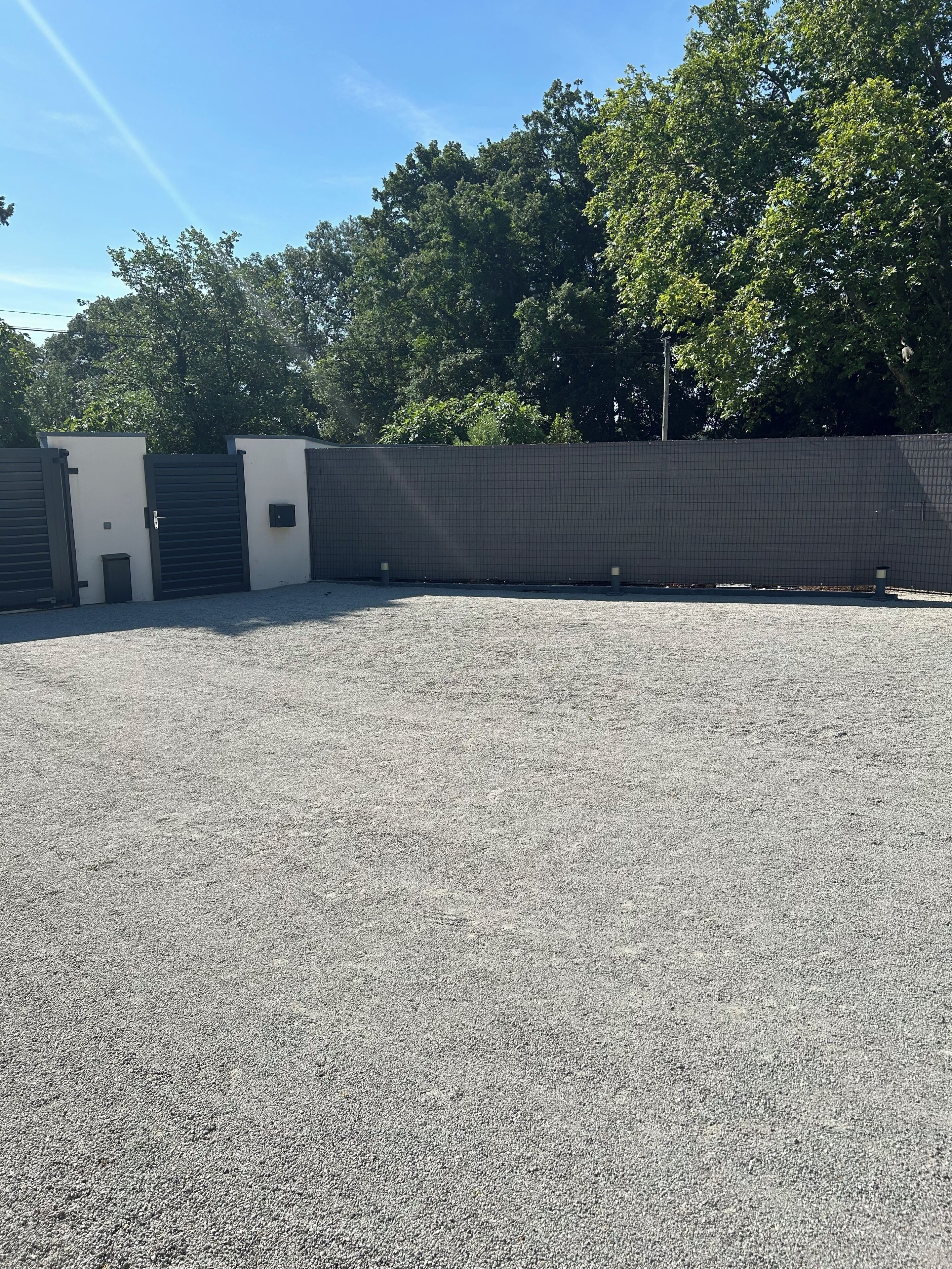 A gravel parking area with a fence and a small building with a door and window.