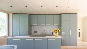 Una cucina moderna con mobili chiari in legno, un'isola centrale e un vaso con fiori.