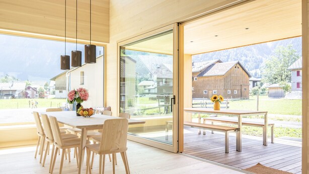 Un'area pranzo moderna con tavolo e sedie in legno, ampie finestre e vista su un paesaggio rurale.