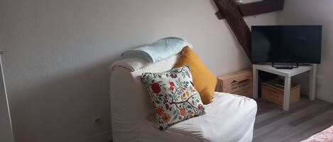 Um quarto aconchegante com um sofá branco, uma televisão sobre um suporte e um vigamento de madeira no teto.