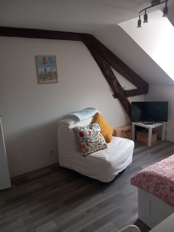Ein gemütliches Zimmer mit einer weißen Couch, einem Fernseher auf einem Schrank und einem Holzbalken an der Decke.