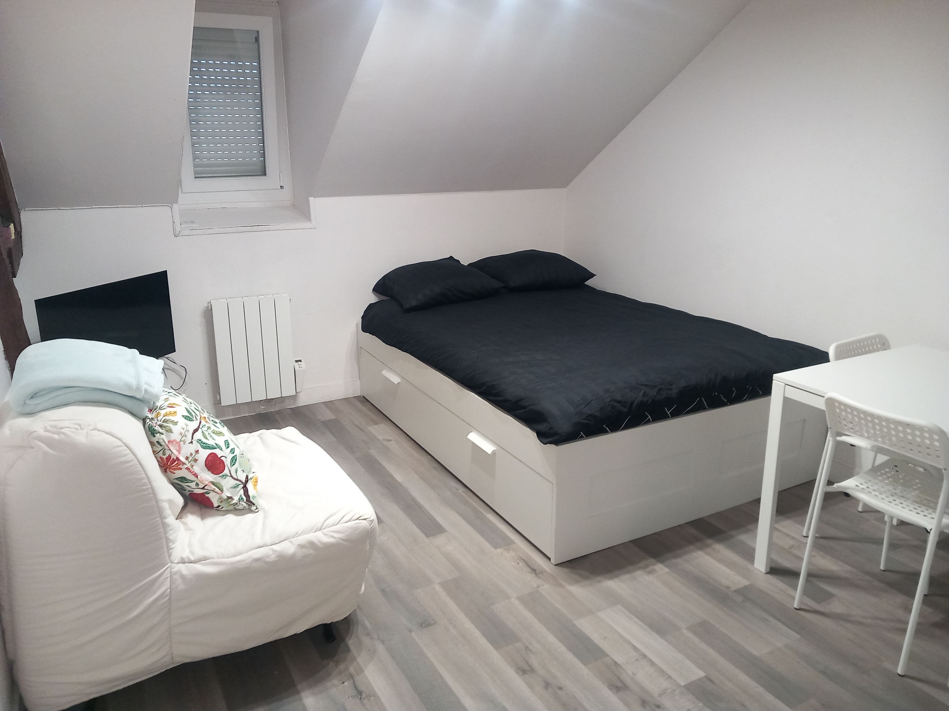Ein Schlafzimmer mit einem Bett, einem Sessel, einem Tisch, einem Heizkörper und einem Fenster.