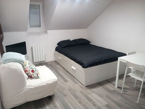 Ein Schlafzimmer mit einem Bett, einem Sessel, einem Tisch, einem Heizkörper und einem Fenster.