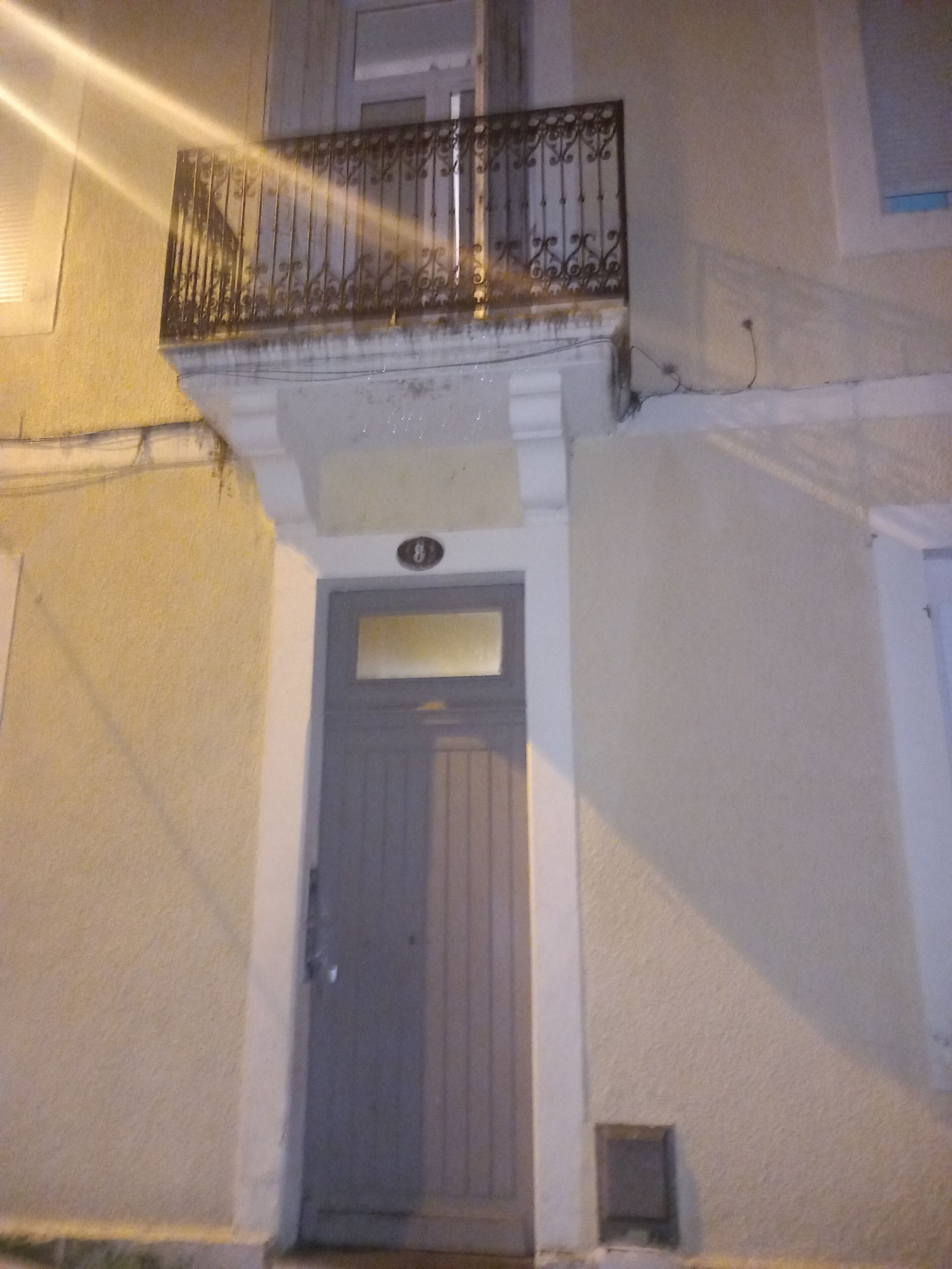 Eine Gebäudefassade mit einer Tür, einem kleinen Fenster und einem Balkon mit Metallgeländer.