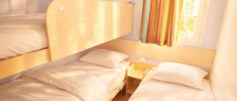 Une chambre avec un lit superposé, une fenêtre, des rideaux et une table de chevet.