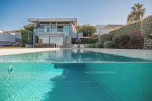 A modern pool area with clear water, a lounge with sunbeds, and a contemporary building in the background. - Kalathas Waterfront Villa (H32M+VR9 Kalathas, Greece)